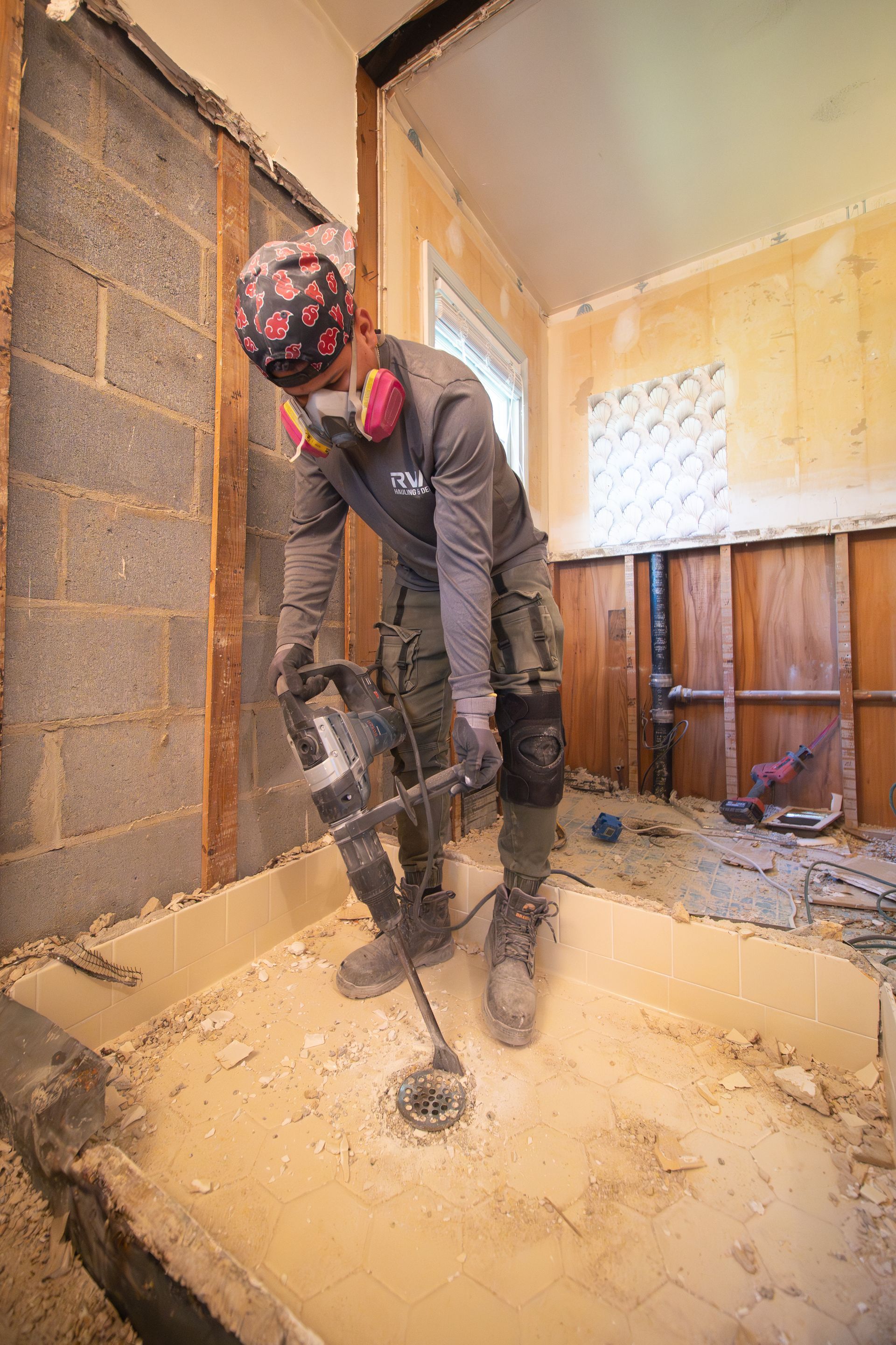 Worker using a jackhammer to break up concrete in a room under renovation