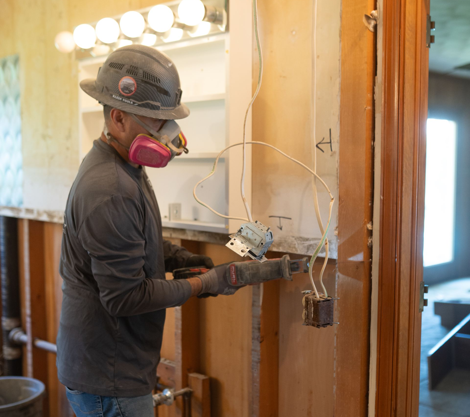 Worker installing wiring on a wall beside a bathroom mirror in a house under renovation
