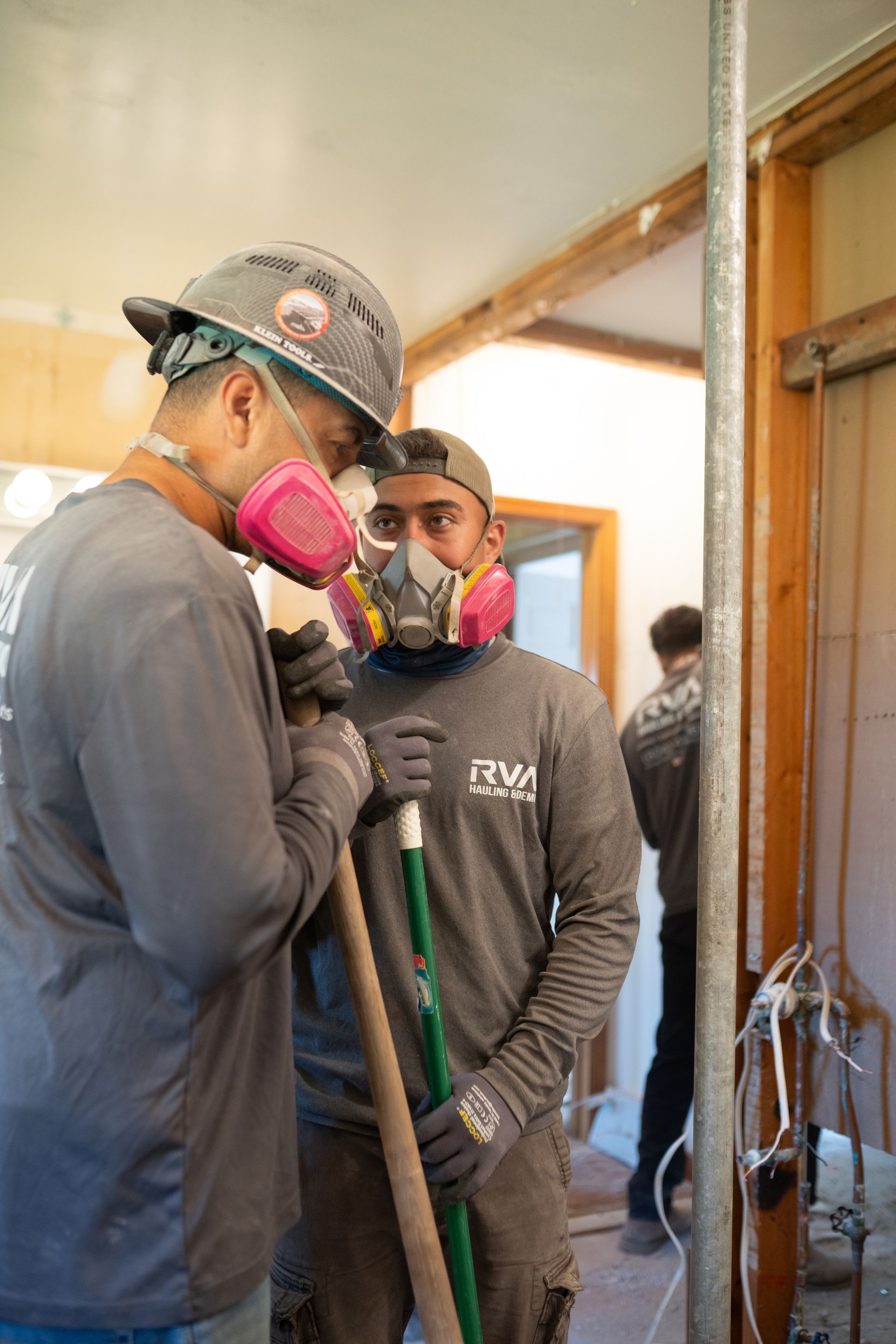 Two workers in hard hats and respirators stand inside a building under construction.
