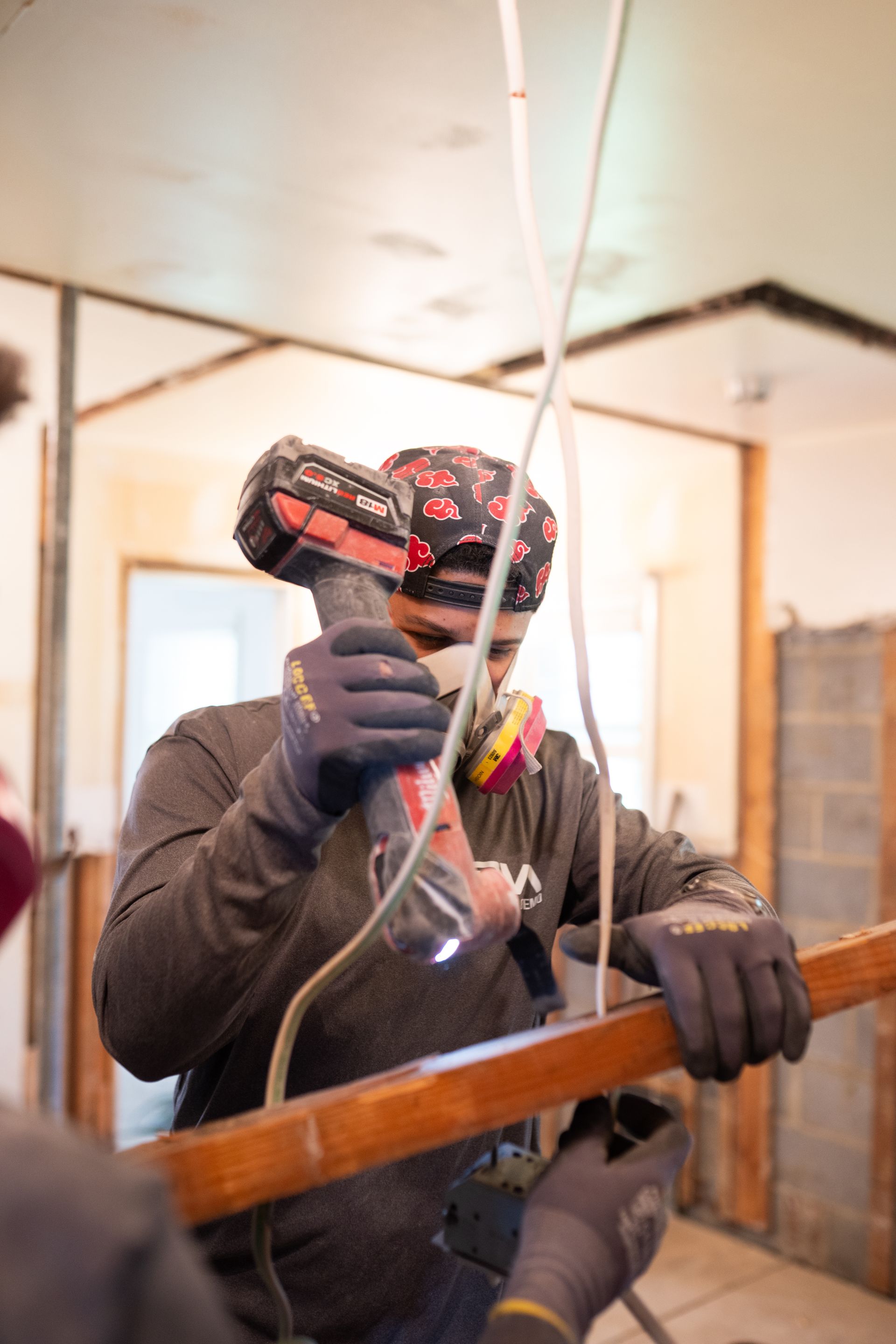 Worker in gloves using a drill to install wiring in an unfinished room.
