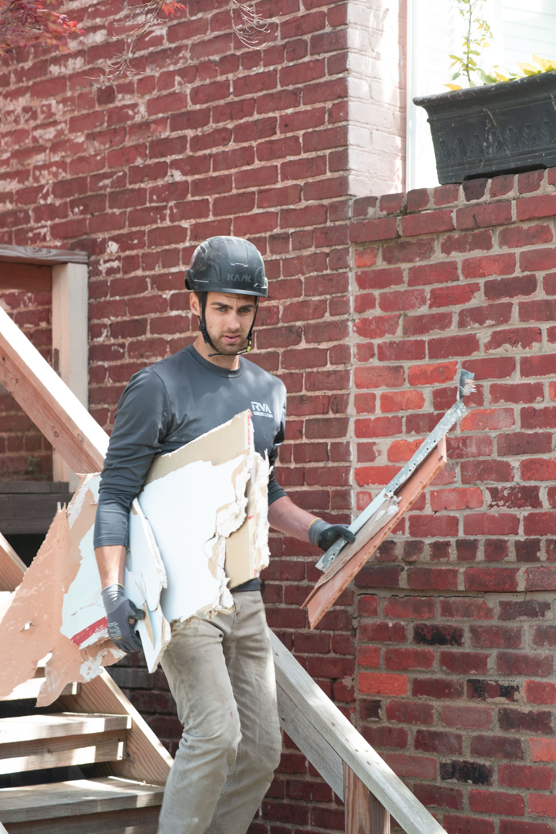 Worker in a hard hat carrying a large white panel on a construction site near a brick wall