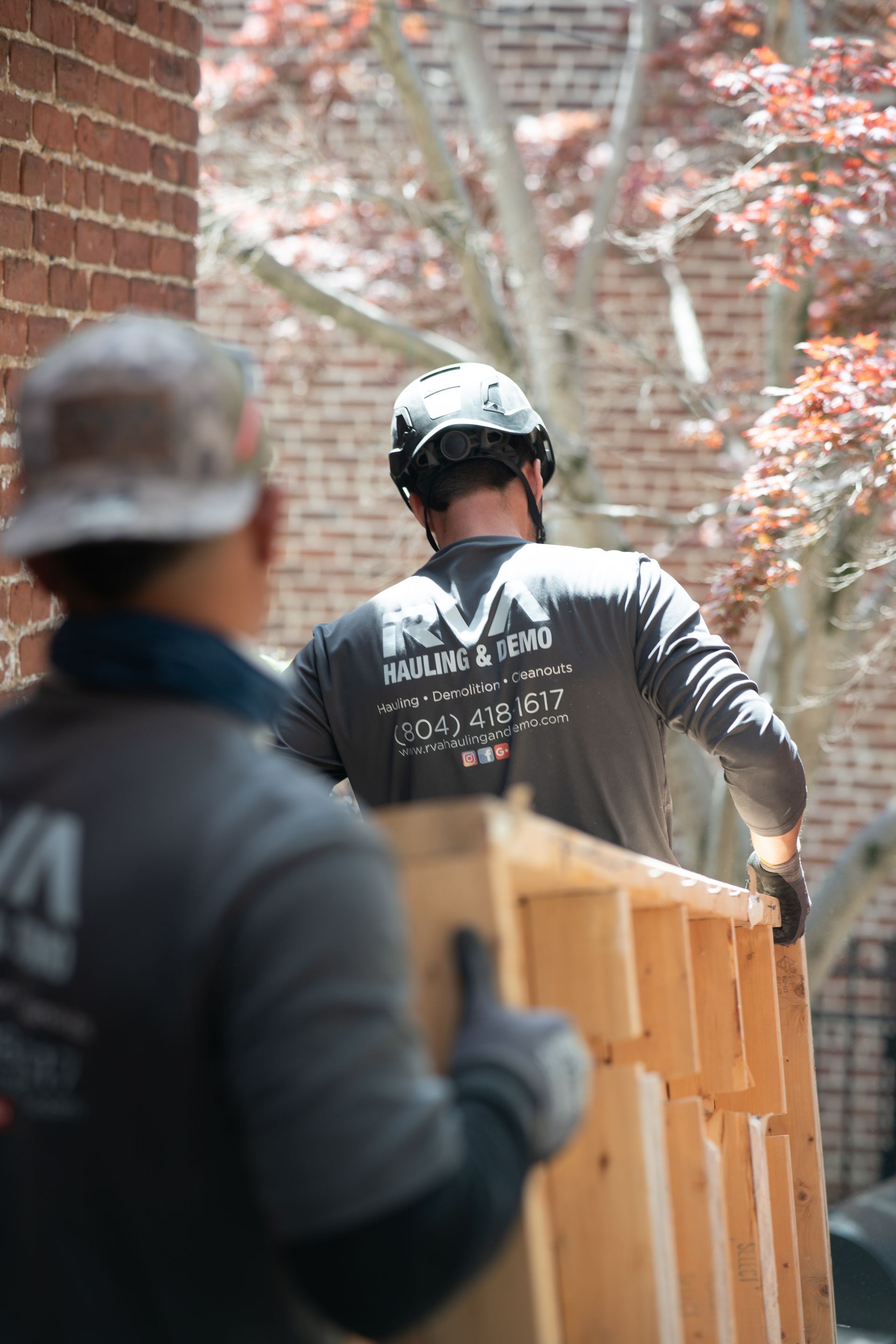 Worker carrying wooden fence panels through a brick-lined alley