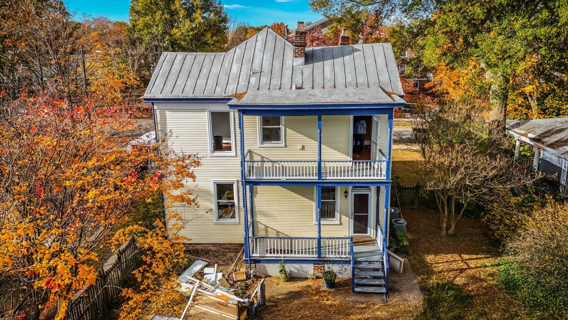 Old white house with blue trim and wraparound porch surrounded by autumn trees