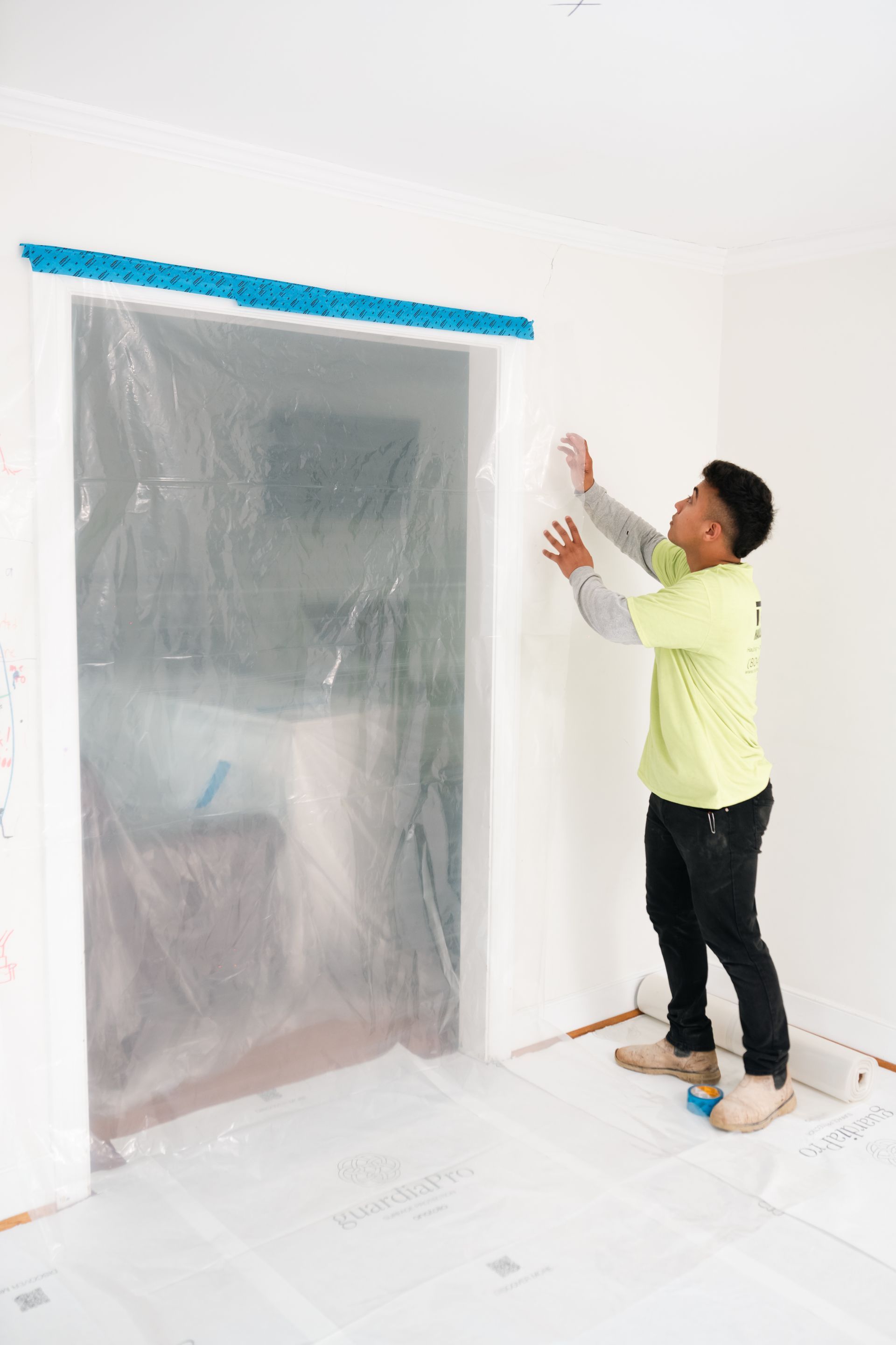 Person applying plastic sheeting over a doorway in a room under renovation