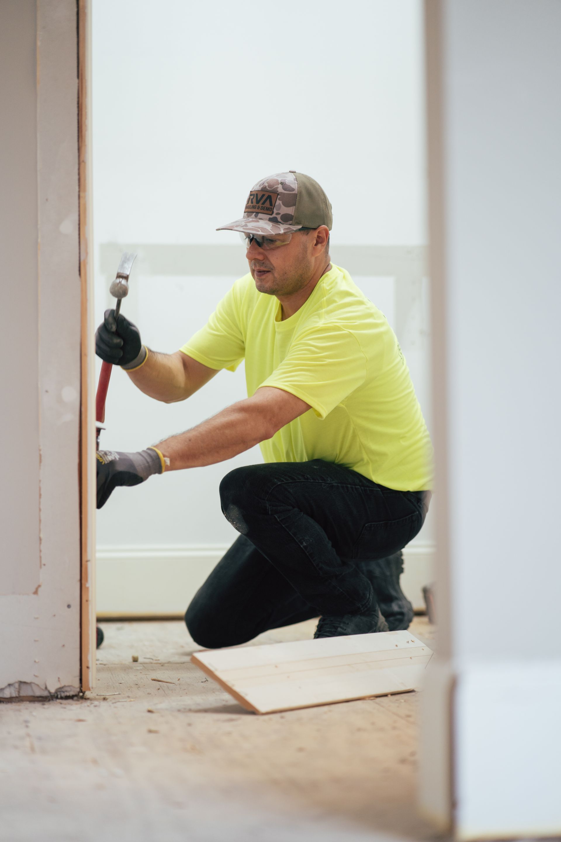 Worker in yellow shirt kneeling with a tool, installing trim in a doorway during home renovation