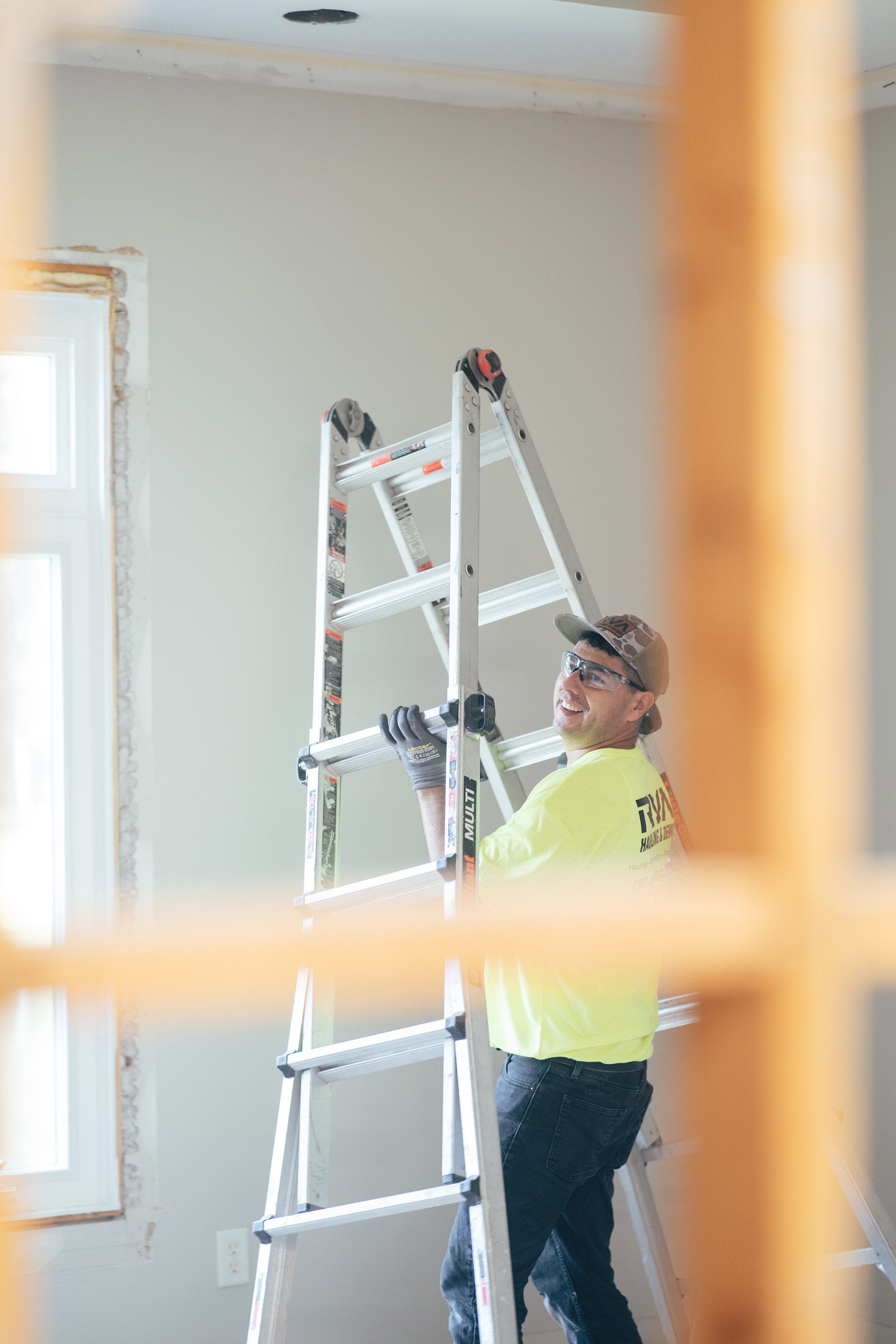 Worker in a neon shirt standing on a ladder in a room being painted.
