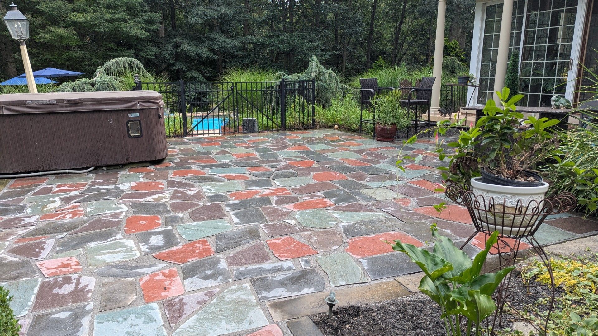 Patio with multi-colored stone, hot tub, small pool, and plants. Overcast day.