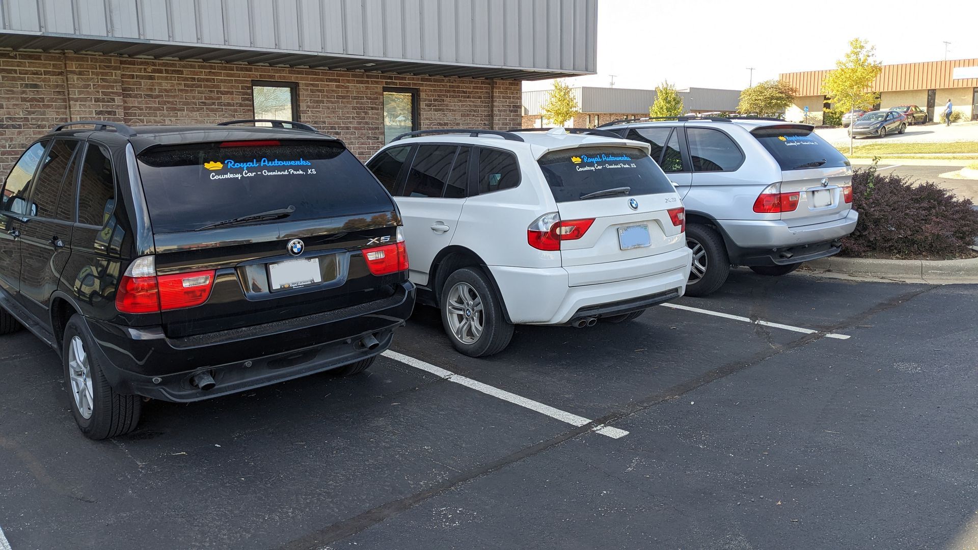 A row of cars are parked in a parking lot in front of a building.