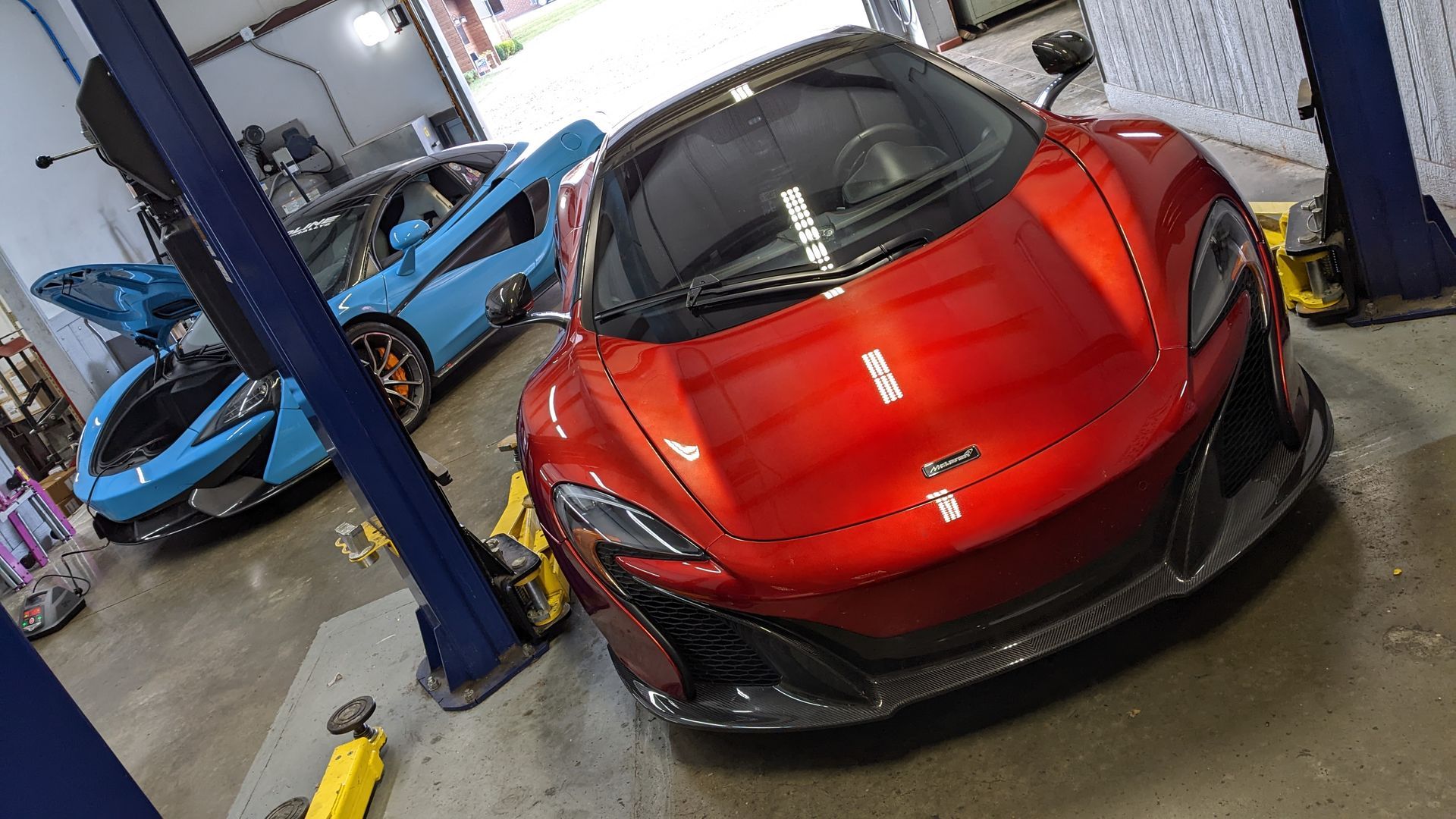 A red sports car is parked in a garage next to a blue sports car.