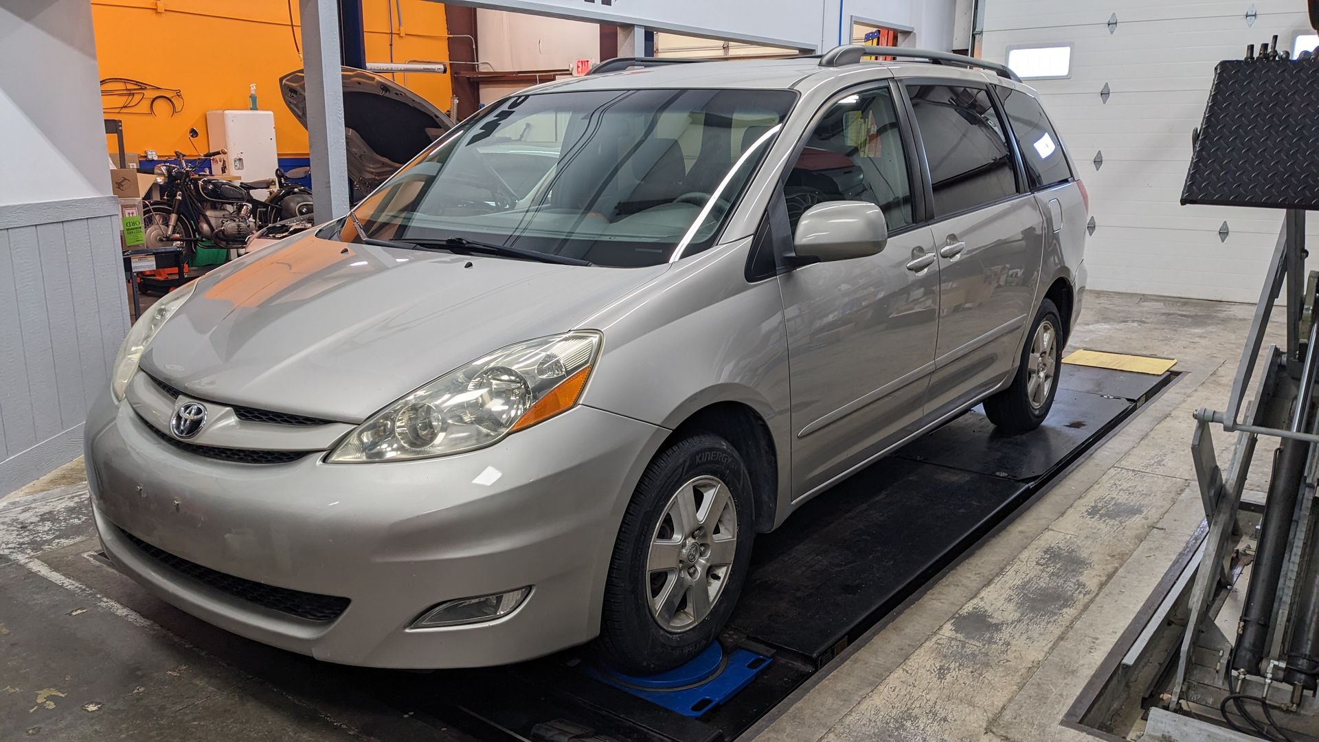 A silver minivan is parked on a lift in a garage.