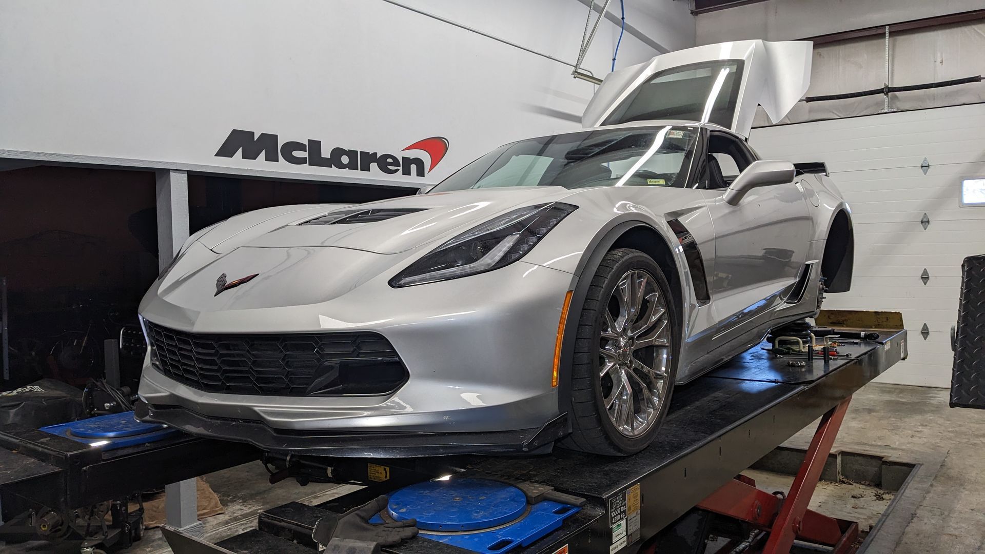 A silver corvette is sitting on a lift in a garage.
