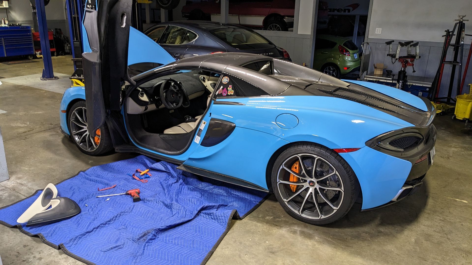 A blue sports car is sitting on a blue tarp in a garage.