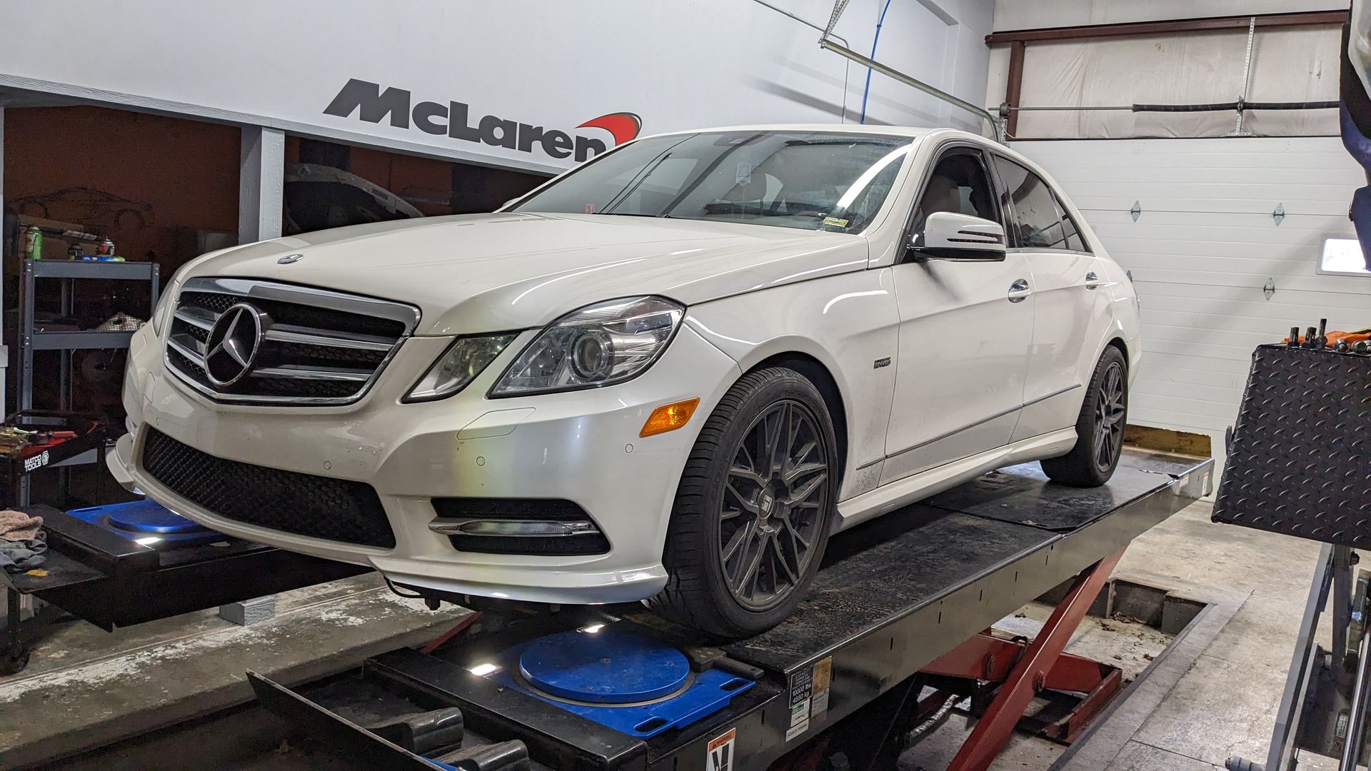 A white mercedes benz is sitting on a lift in a garage.