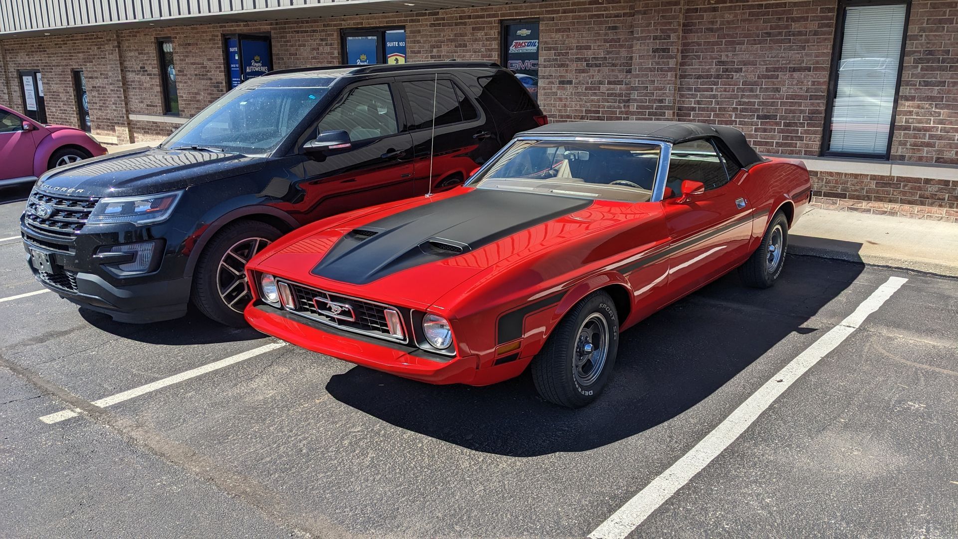 A red mustang convertible is parked in a parking lot next to a black suv.