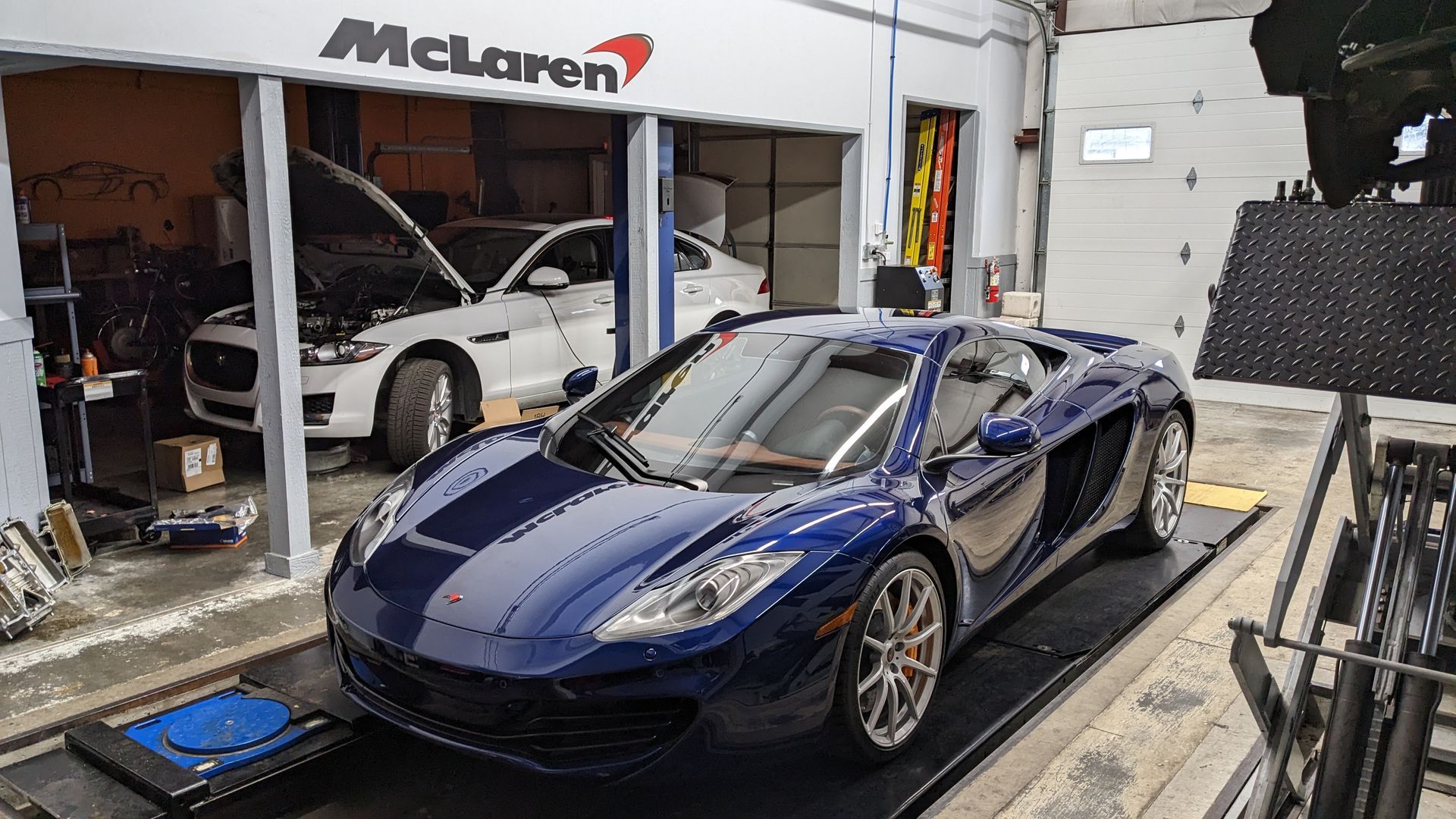 A blue sports car is parked in front of a mclaren garage.