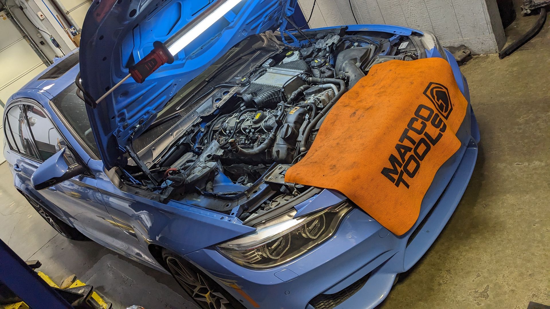 A blue car with the hood open is being worked on in a garage.