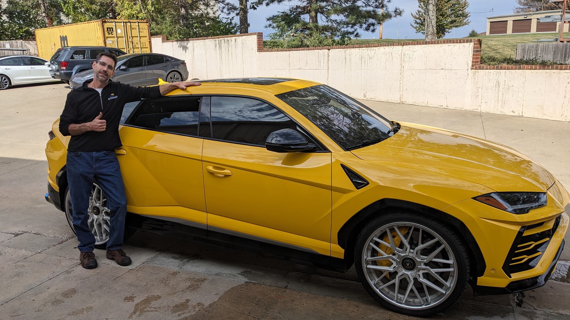 A man is standing next to a yellow car in a parking lot.