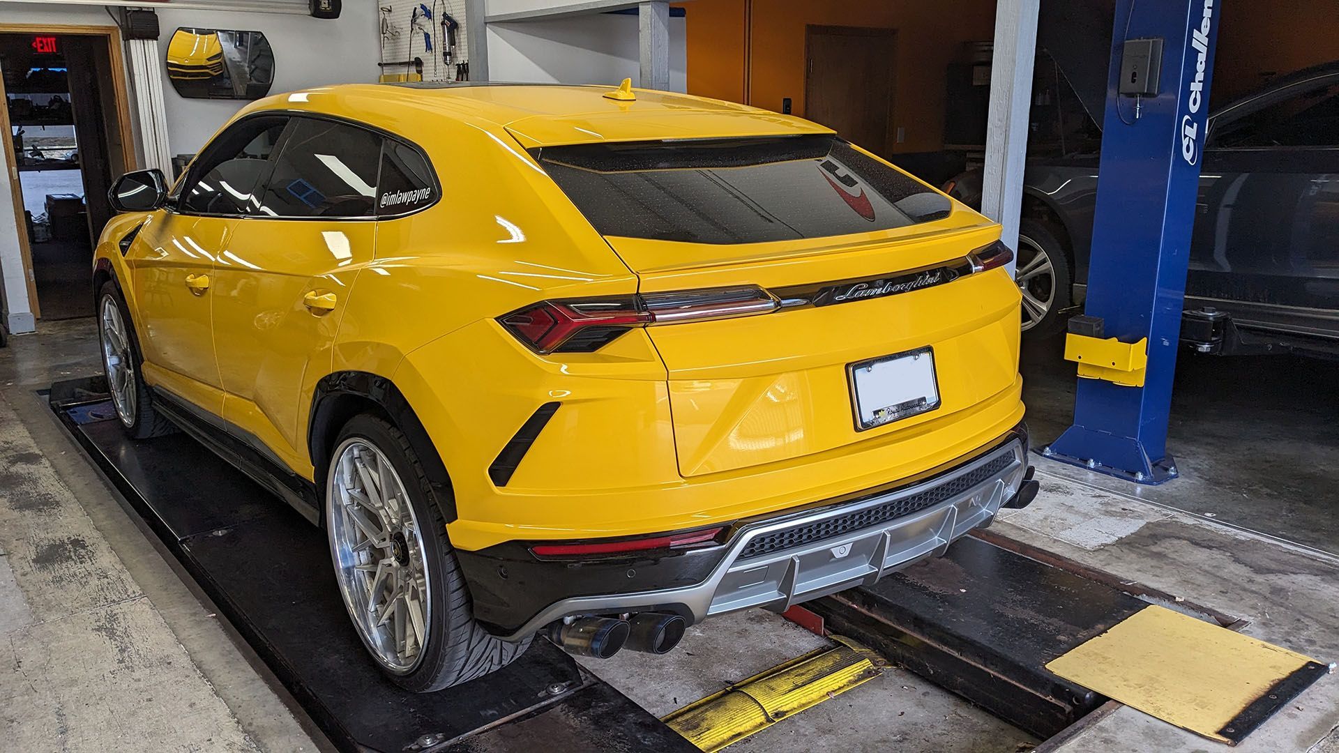 A yellow lamborghini urus is sitting on a lift in a garage.