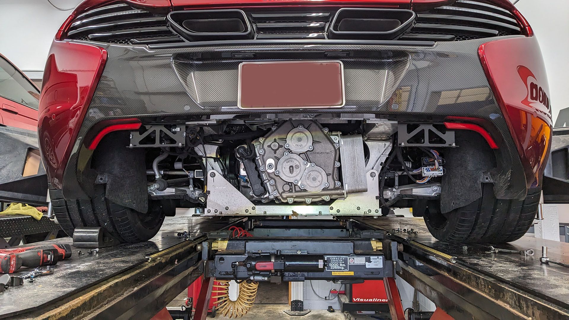 A red sports car is sitting on a lift in a garage.