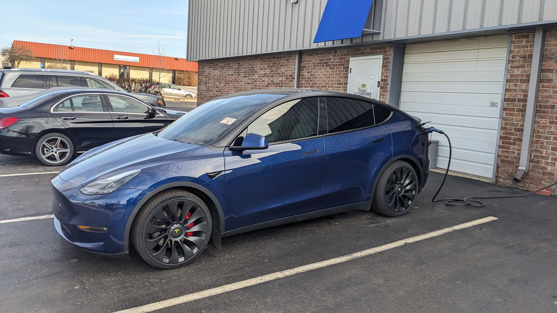 A blue tesla model y is being charged in a parking lot.