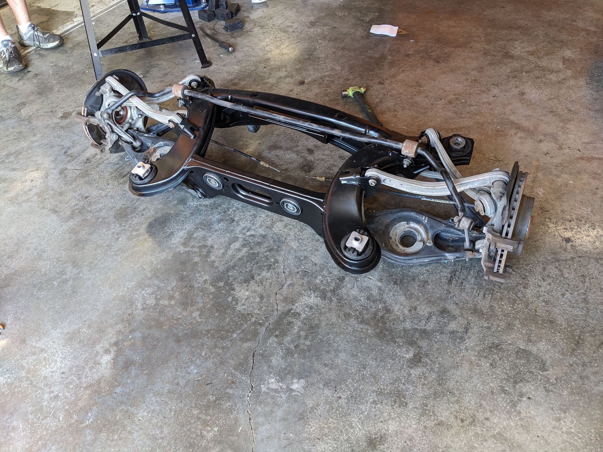 A car chassis is laying on the ground in a garage.