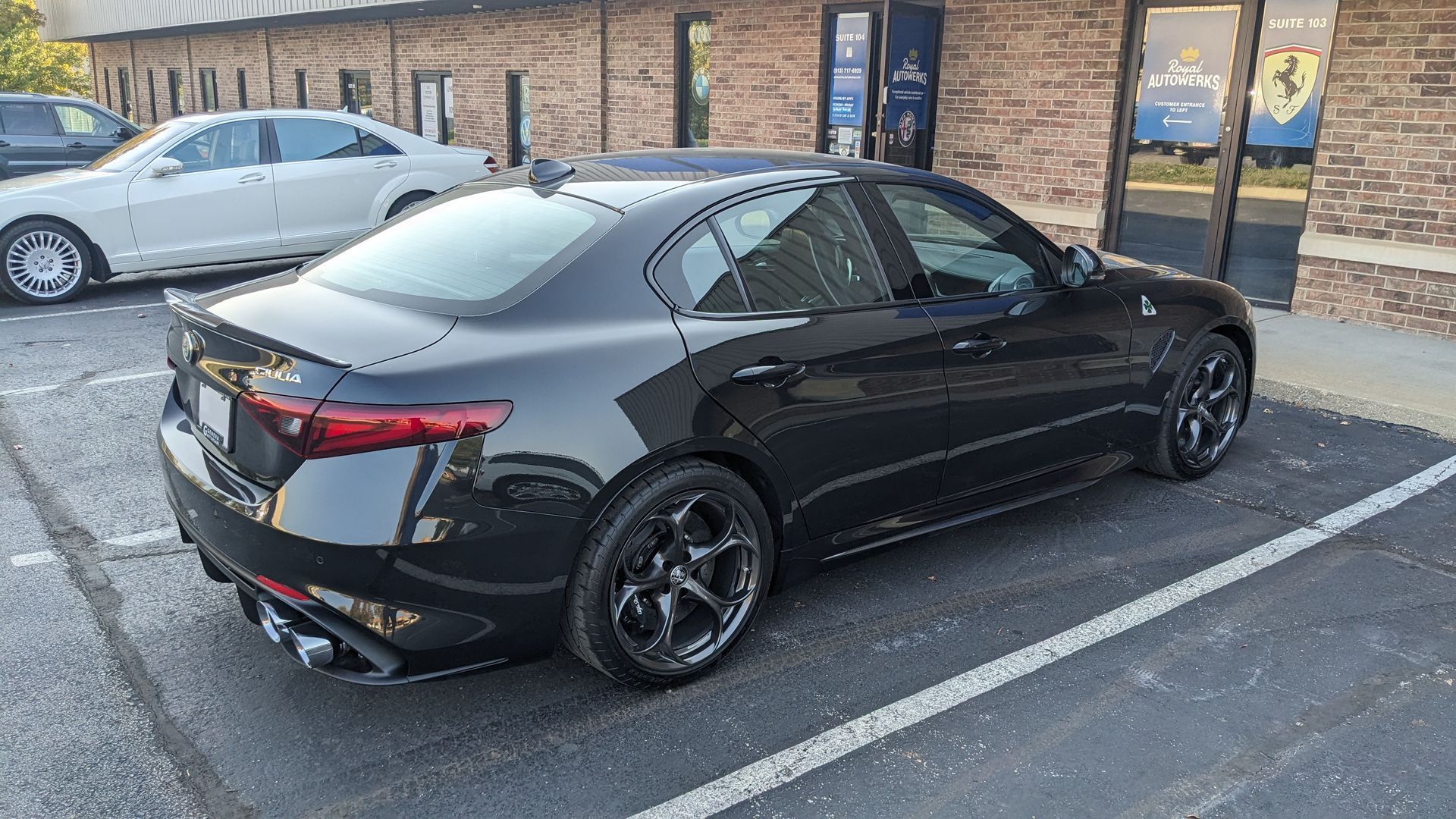 A black car is parked in a parking lot in front of a brick building.