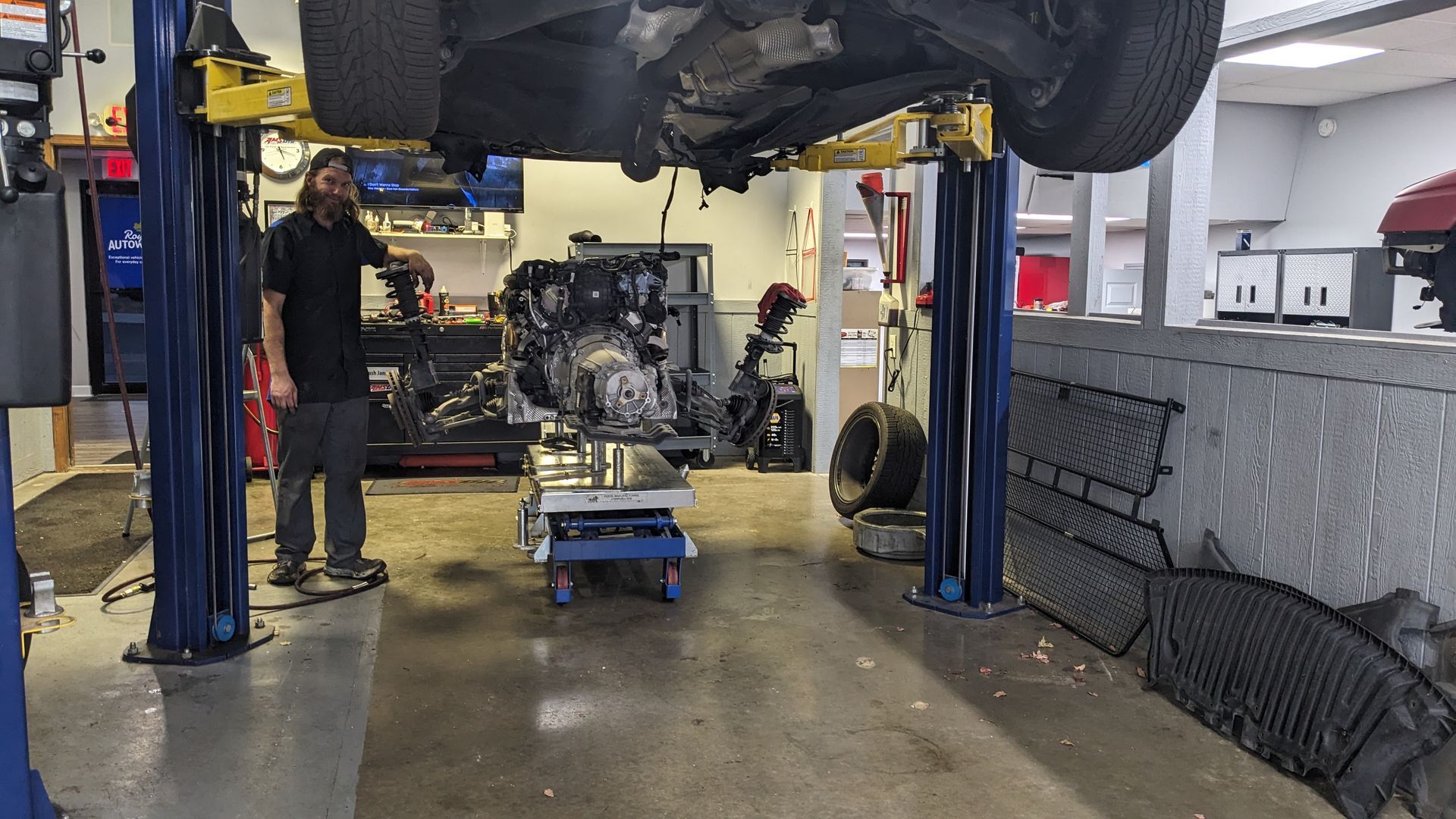 A man is standing next to a car on a lift in a garage.