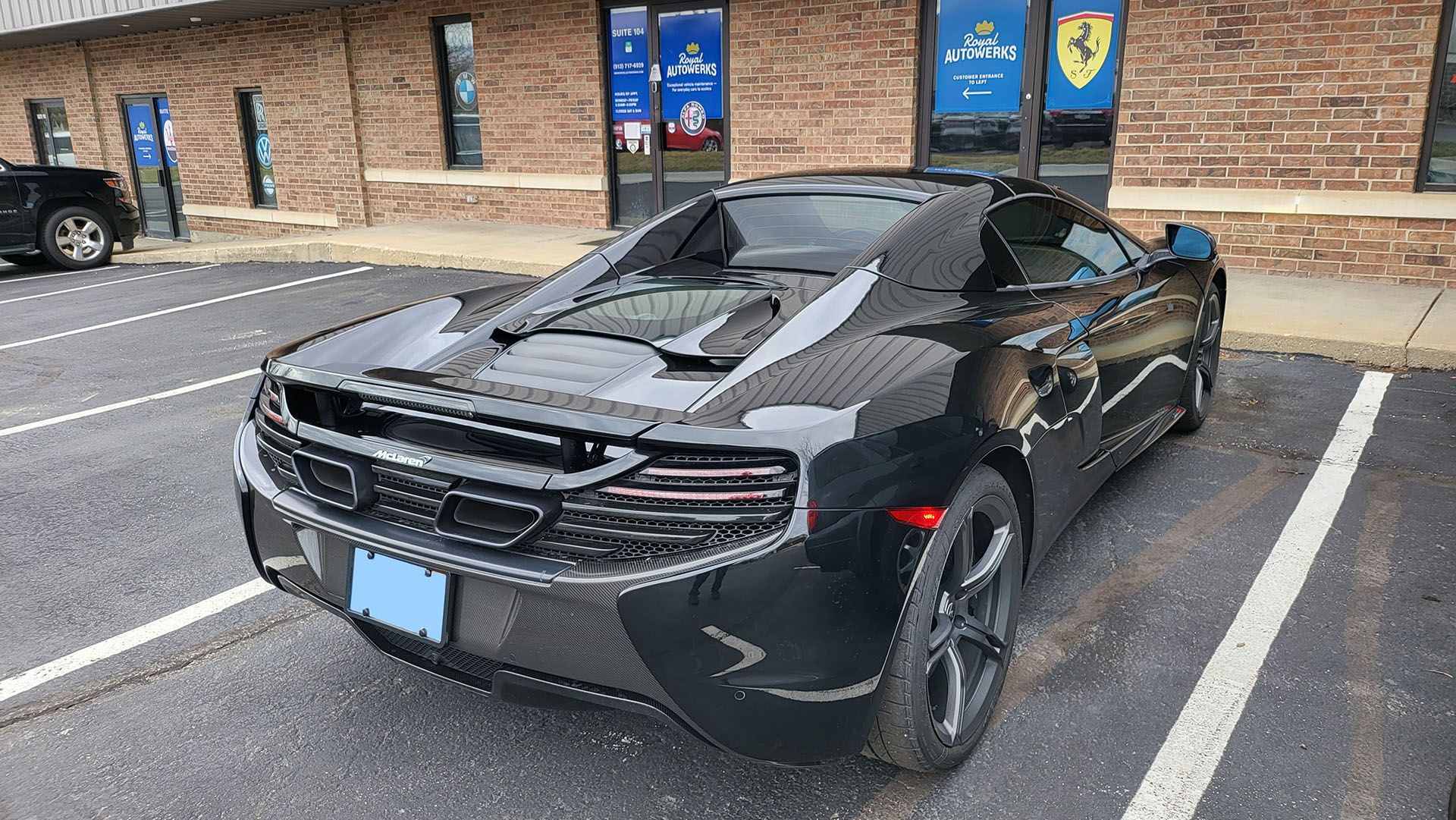 A black sports car is parked in a parking lot in front of a brick building.