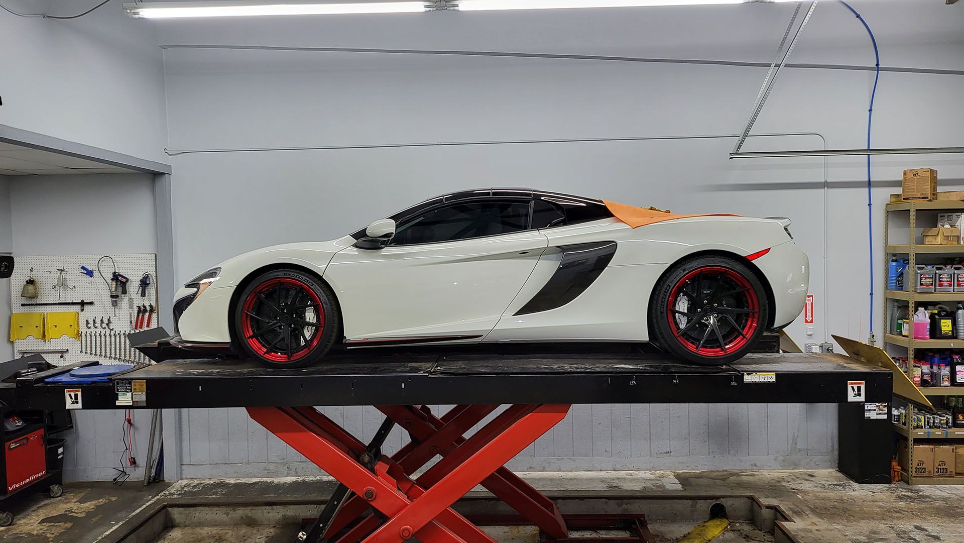A white sports car is parked on a lift in a garage.