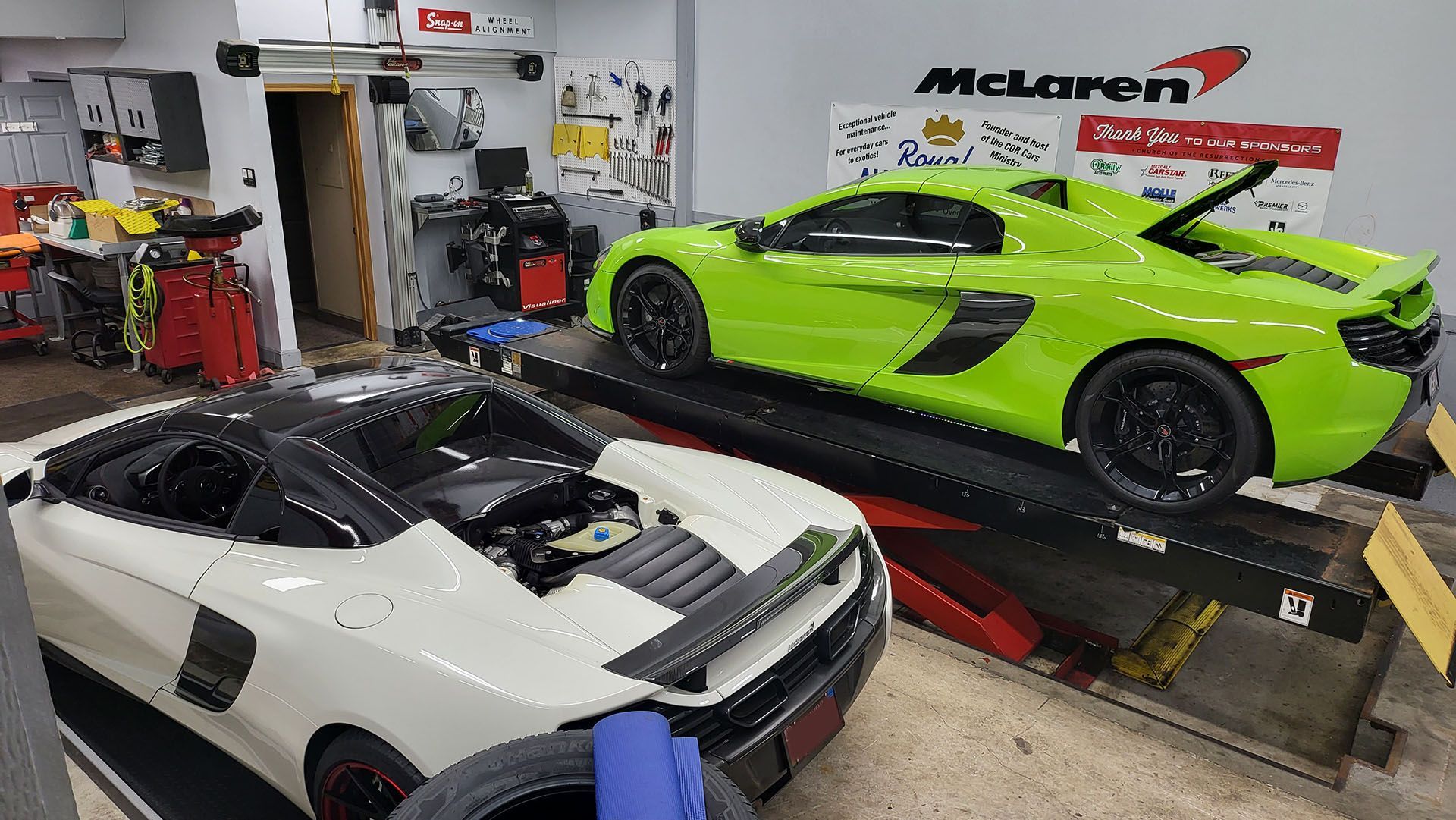 A green and a white sports car are parked next to each other in a garage.