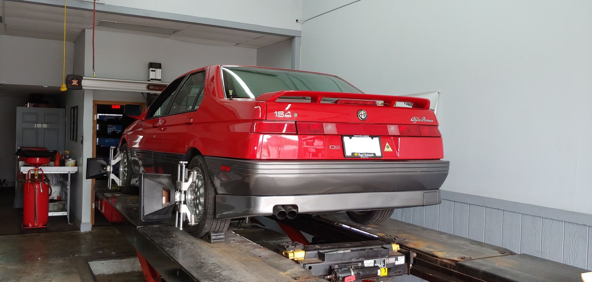 A red car is sitting on a lift in a garage.