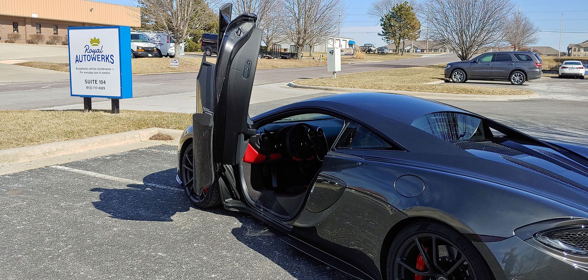 A black sports car is parked in a parking lot with its door open.