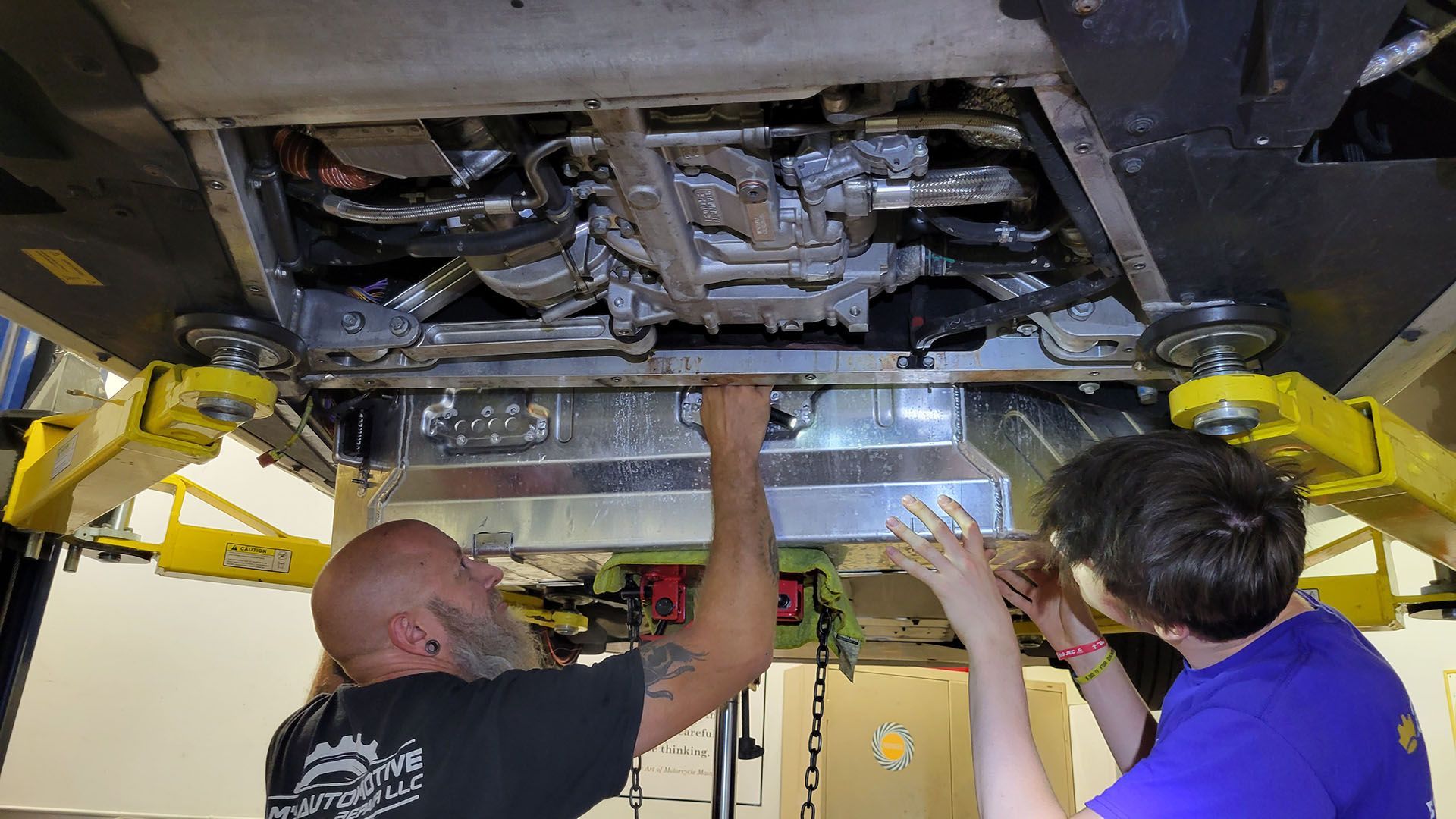 Two men are working under a car in a garage.