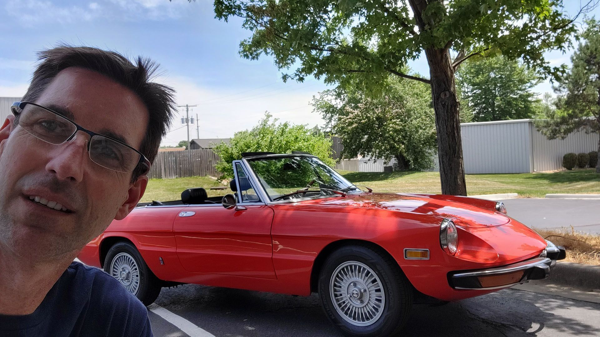 A man is taking a selfie in front of a red sports car.