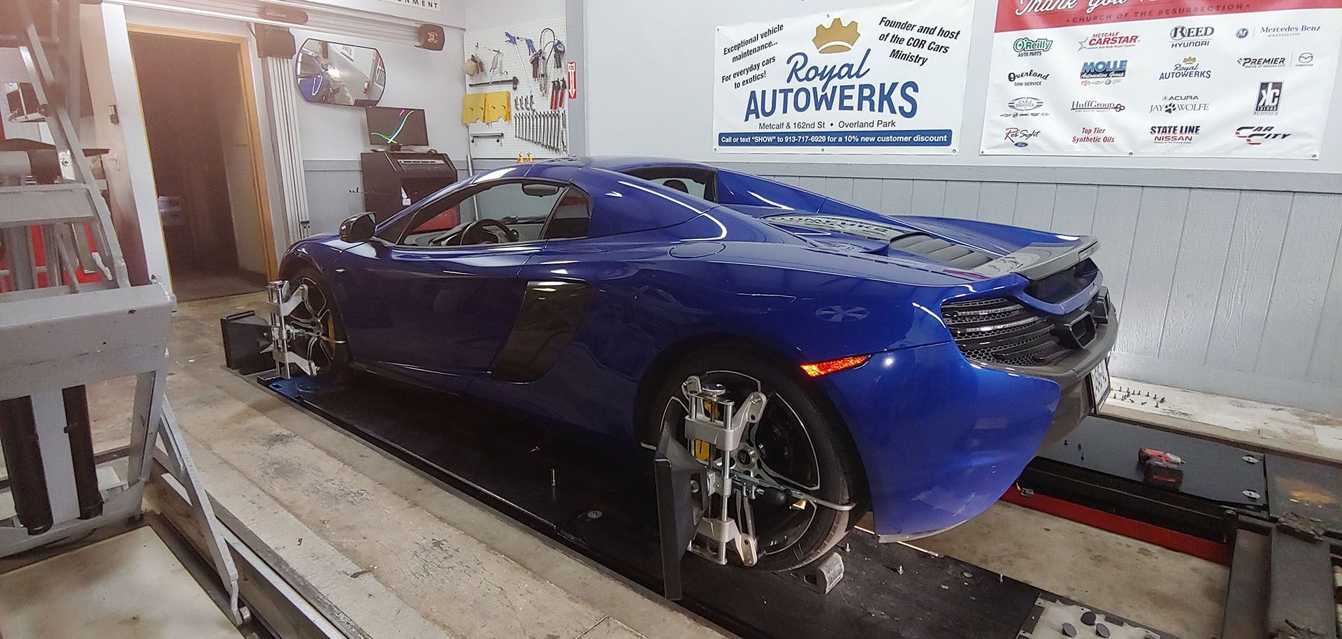 A blue sports car is sitting on a lift in a garage.