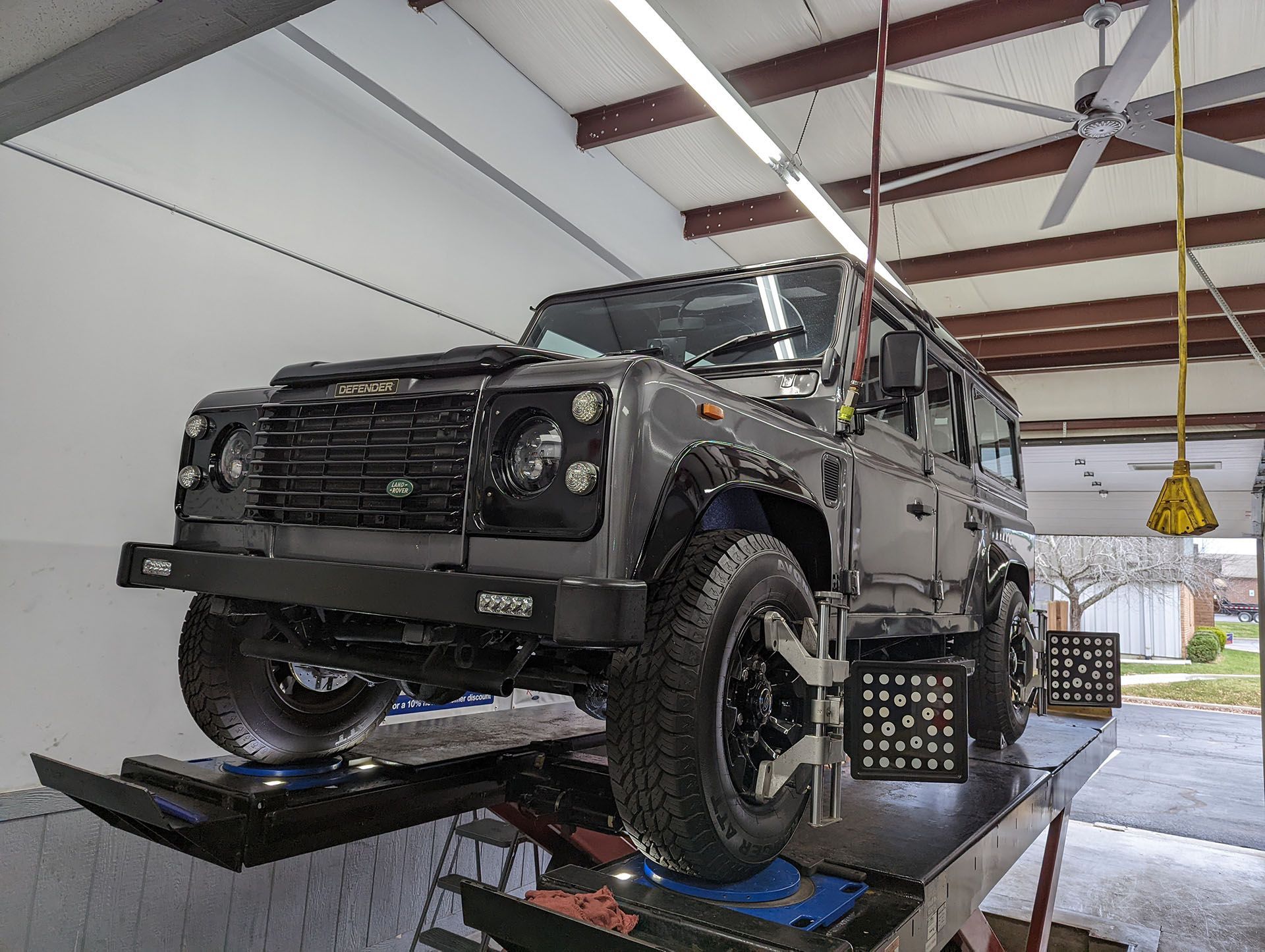 A gray jeep is sitting on a lift in a garage.