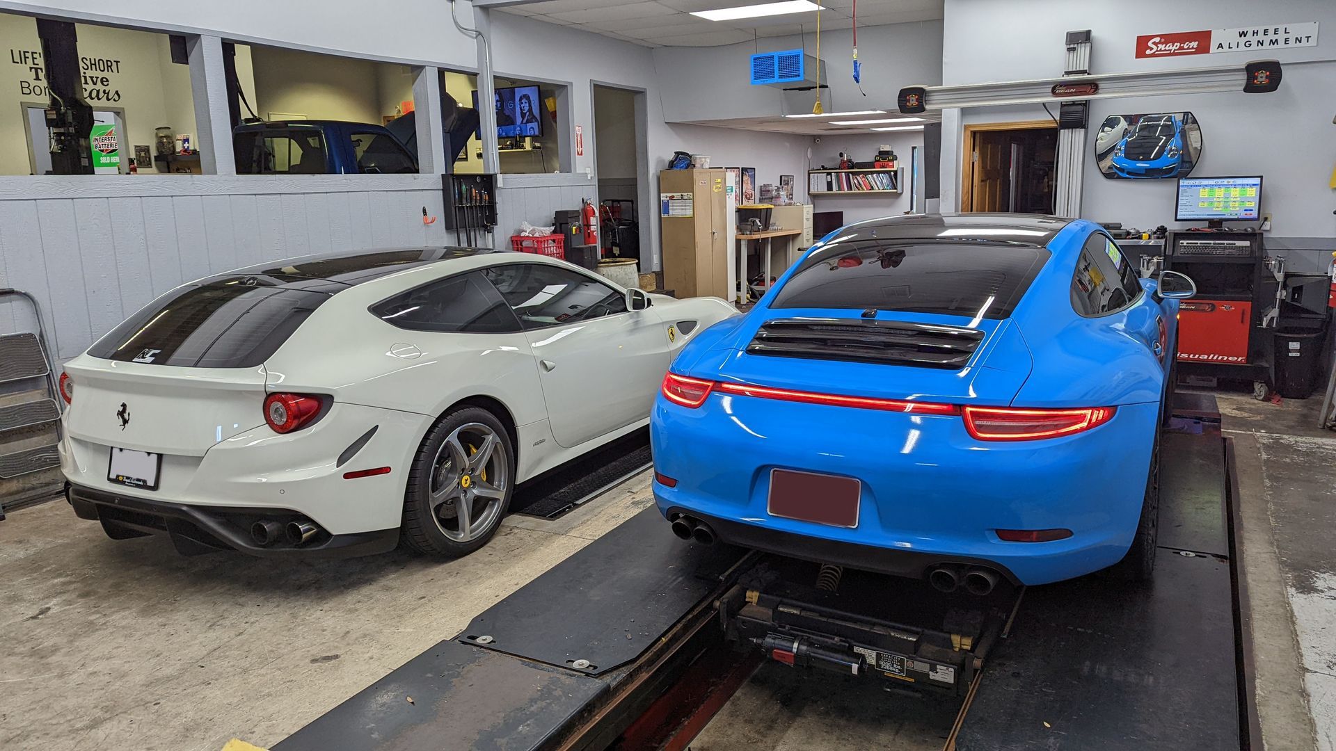 Two sports cars are sitting on a lift in a garage.