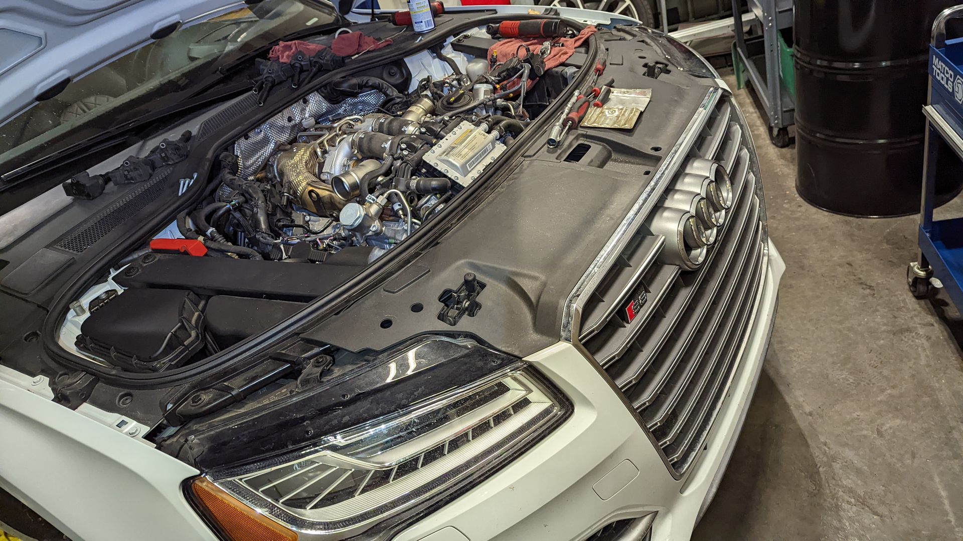 A white car with the hood open in a garage.
