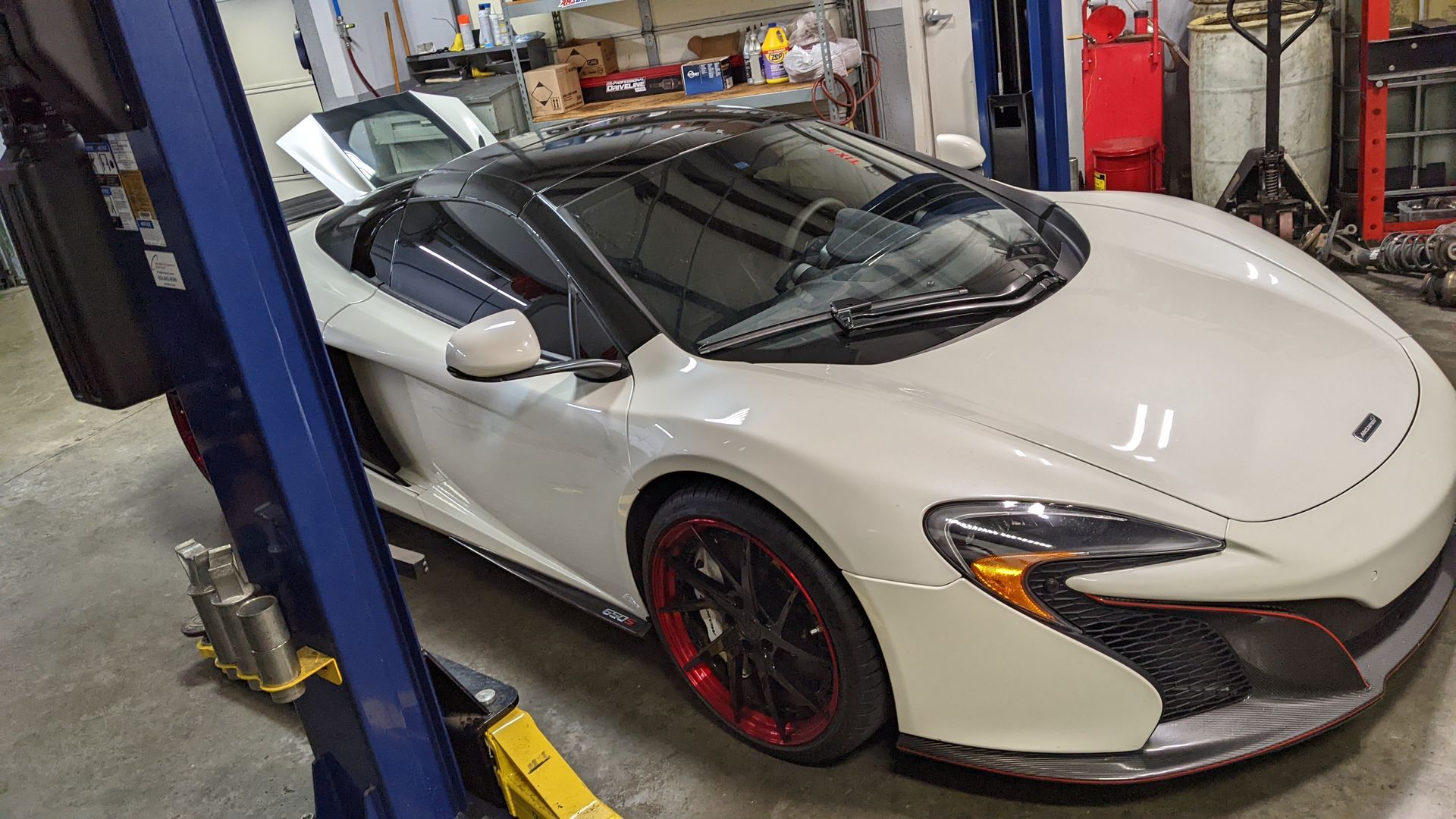 A white sports car is on a lift in a garage.