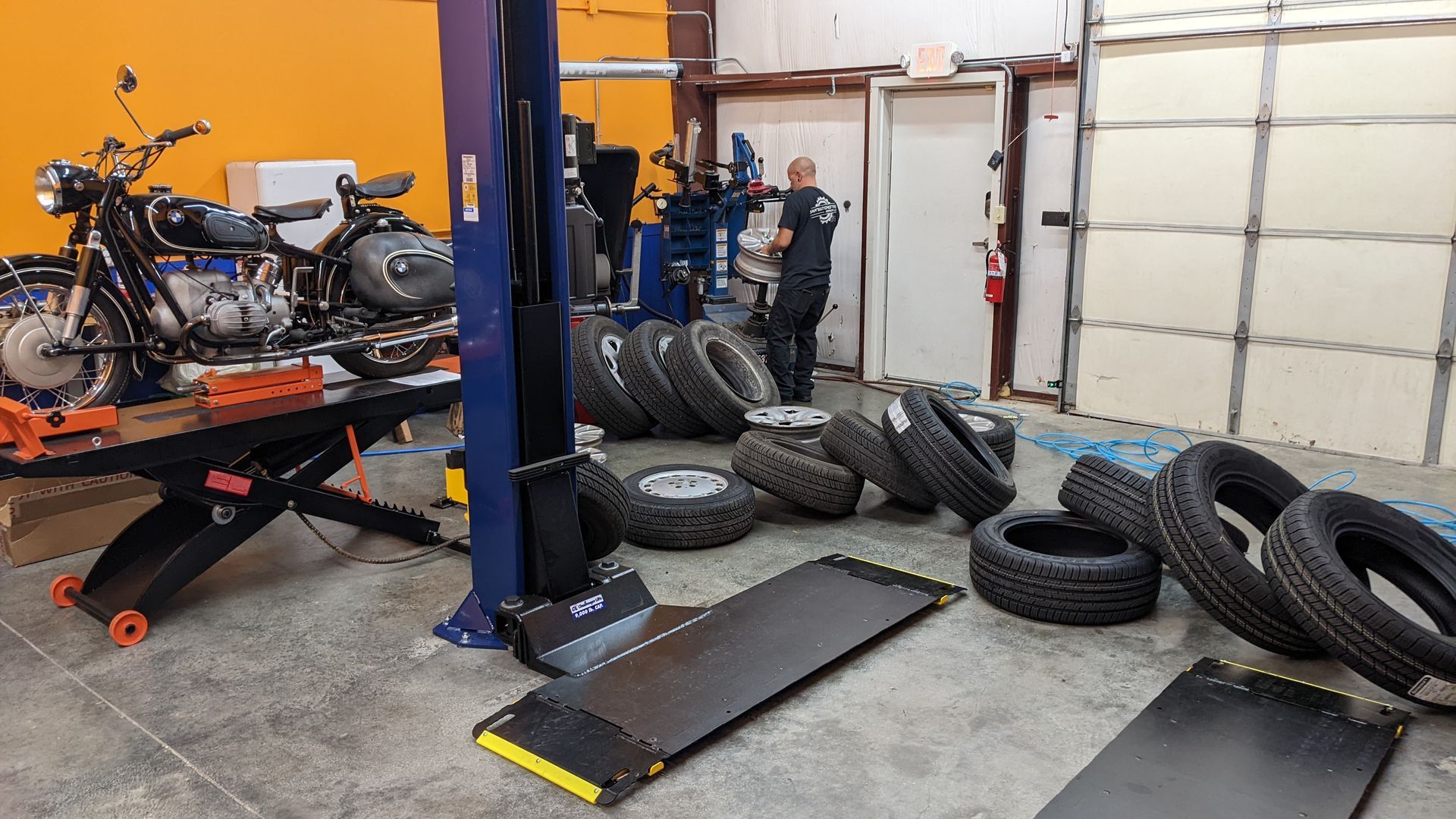 A motorcycle is sitting on a lift in a garage next to a pile of tires.
