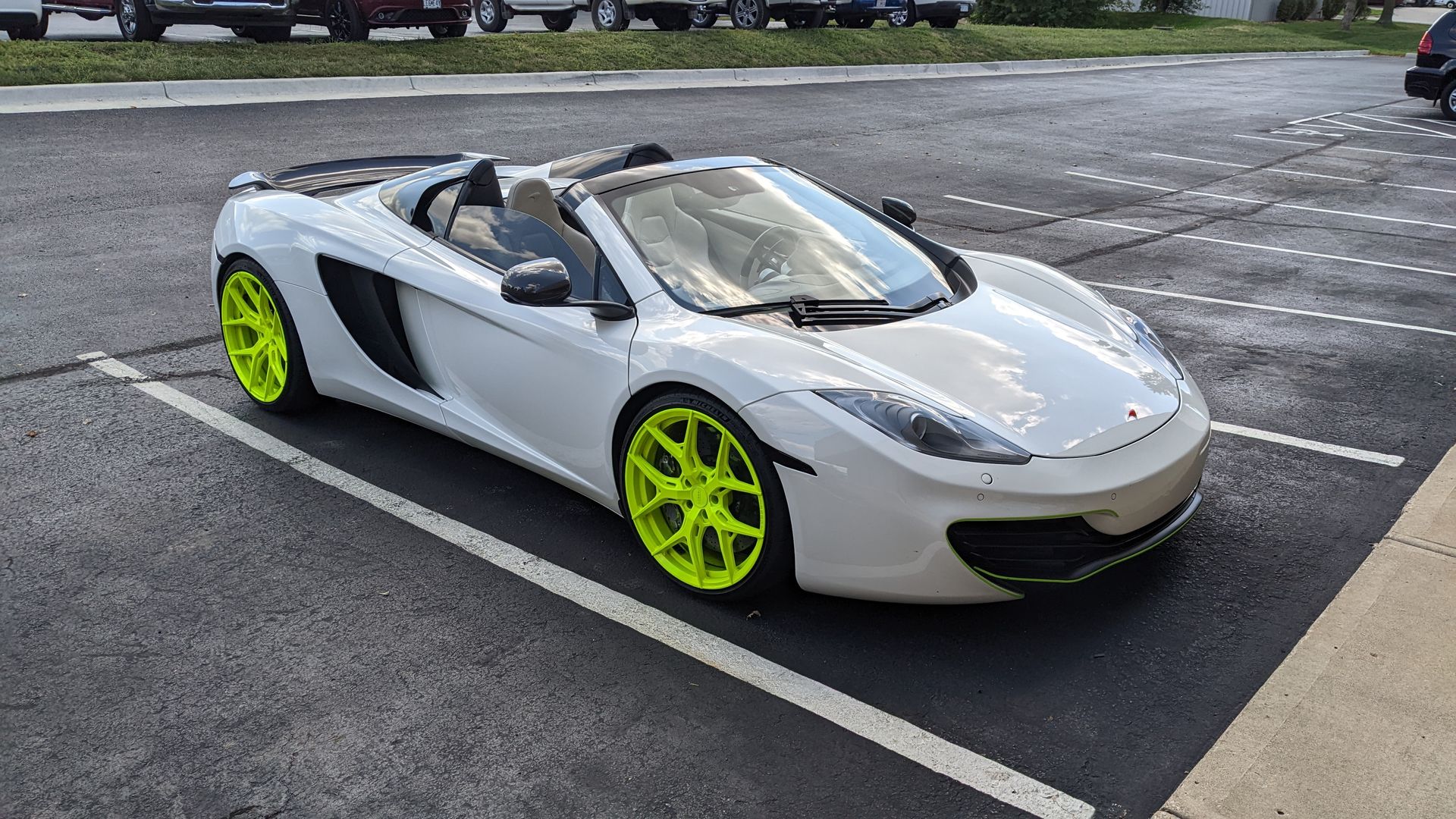 A white sports car with neon yellow wheels is parked in a parking lot.