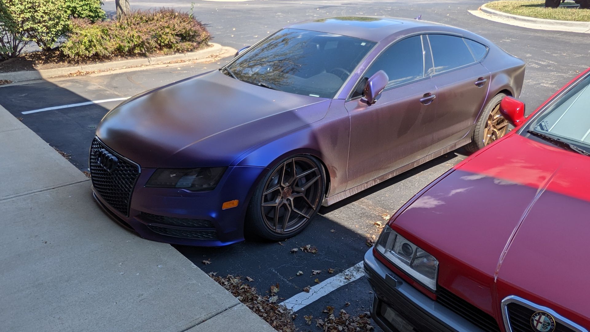 A purple car is parked next to a red car in a parking lot.