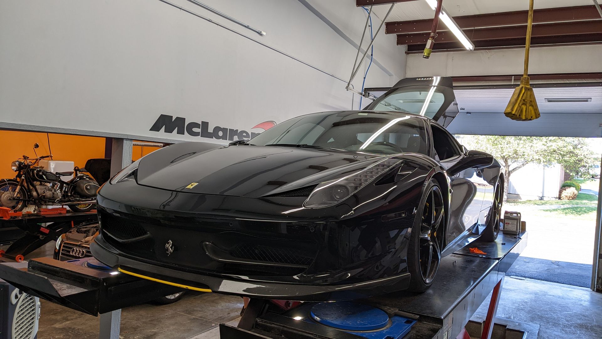 A black ferrari is sitting on a lift in a garage.