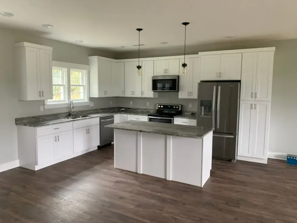White kitchen with gray countertops, island, and stainless steel appliances; dark wood flooring.