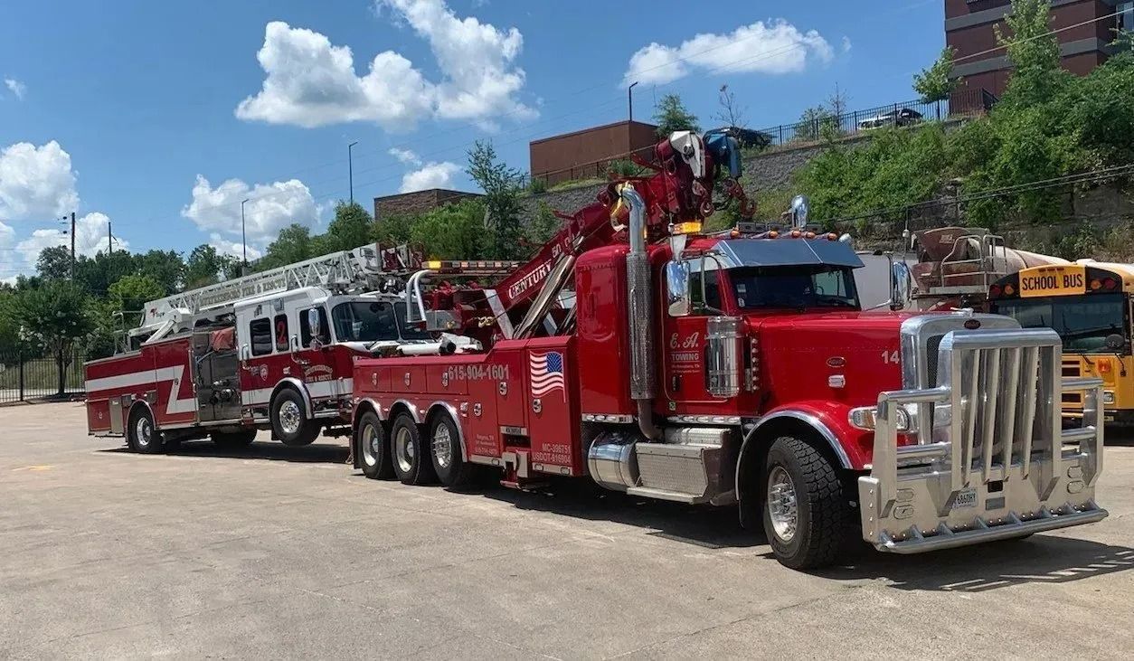 Red tow truck hauling a fire truck on a sunny day.