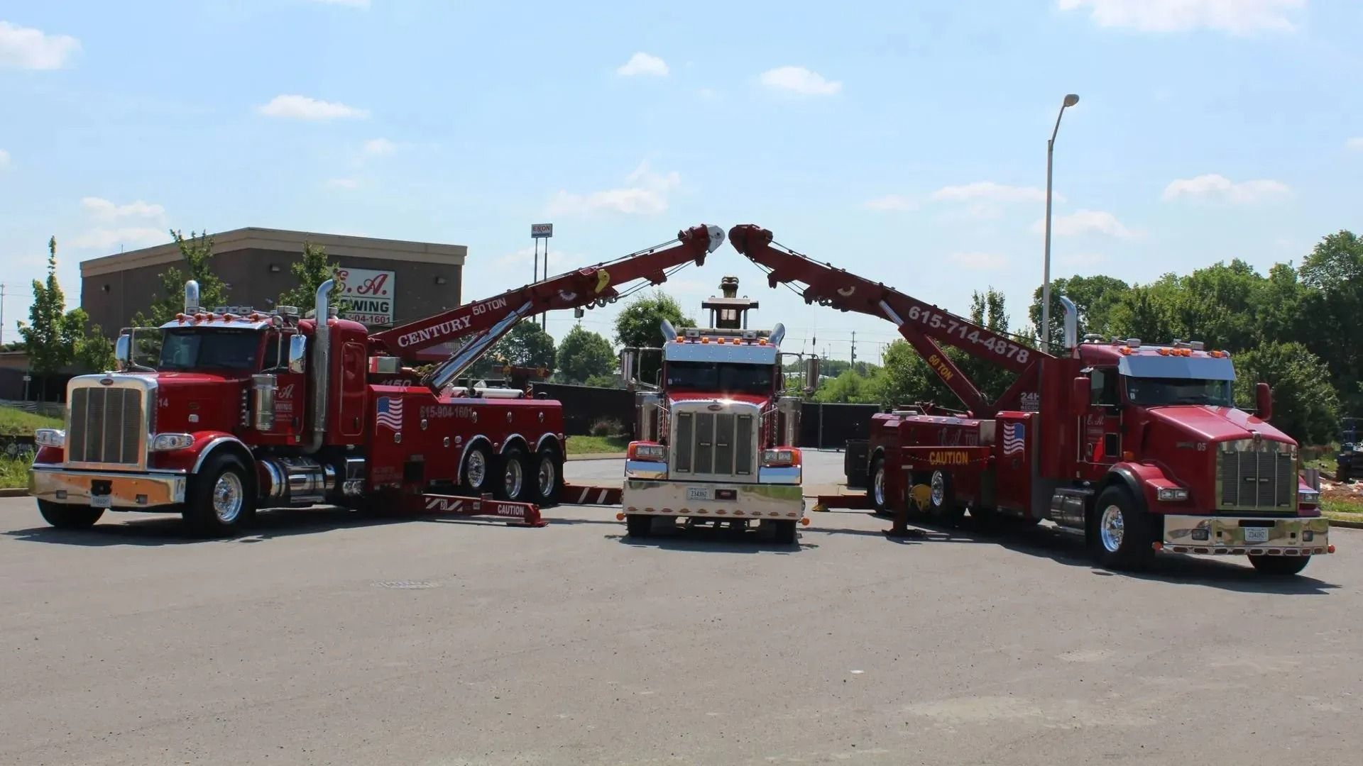 Three red tow trucks parked outside on a sunny day. The booms are raised, and the scene appears to be an advertising shot.