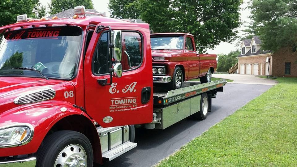 Red tow truck carrying a classic brown pickup truck on a sunny day.
