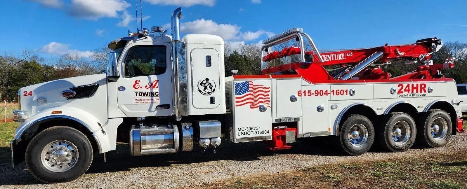 White tow truck with red accents, American flag graphic, under blue sky.