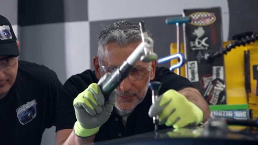 Two men are working on a car in a garage.
