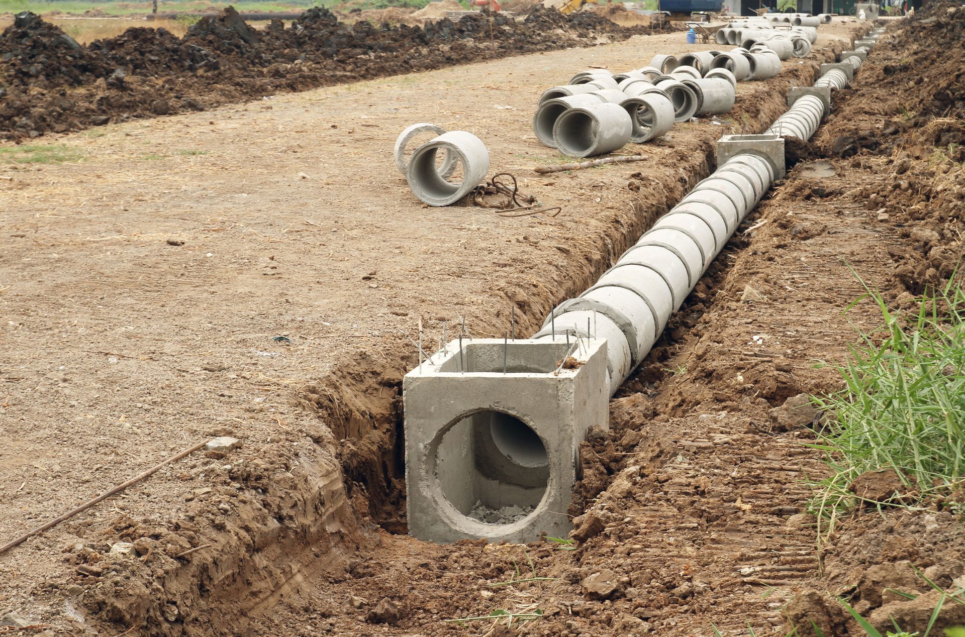 Construction site: concrete culvert pipes being installed in a trench alongside a dirt road.